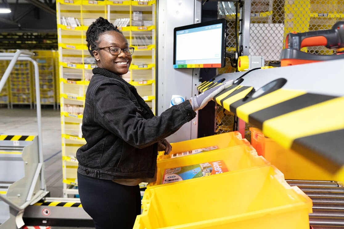An Amazon employee smile as she works in a fulfillment center sorting through products.