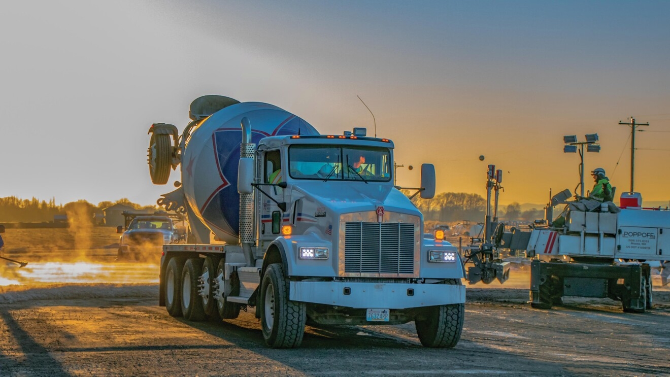 An image of a concrete truck on a construction field with a sunset in the background. 
