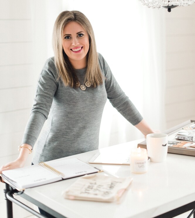 A woman small business owner smiles at the camera as she leans against a tabletop.