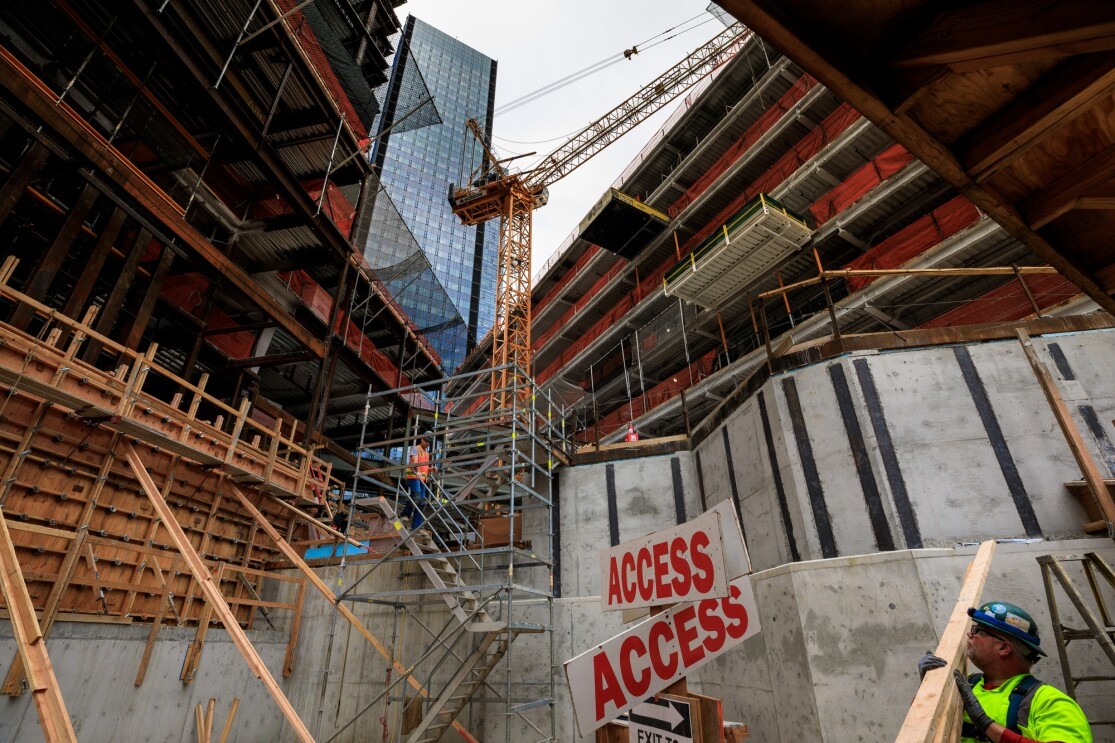 Buildings under construction on Amazon's South Lake Union campus. A construction worker carries 2x4s next to an "access" sign. A temporary staircase is in place near a crane.