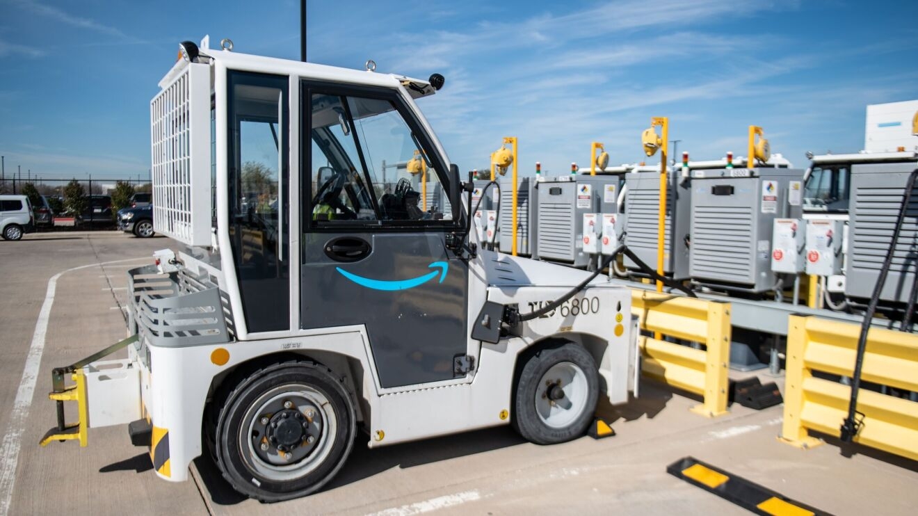 An image of a small vehicle used to move packages. It is on a charger at a charging station at an Amazon Air Hub.