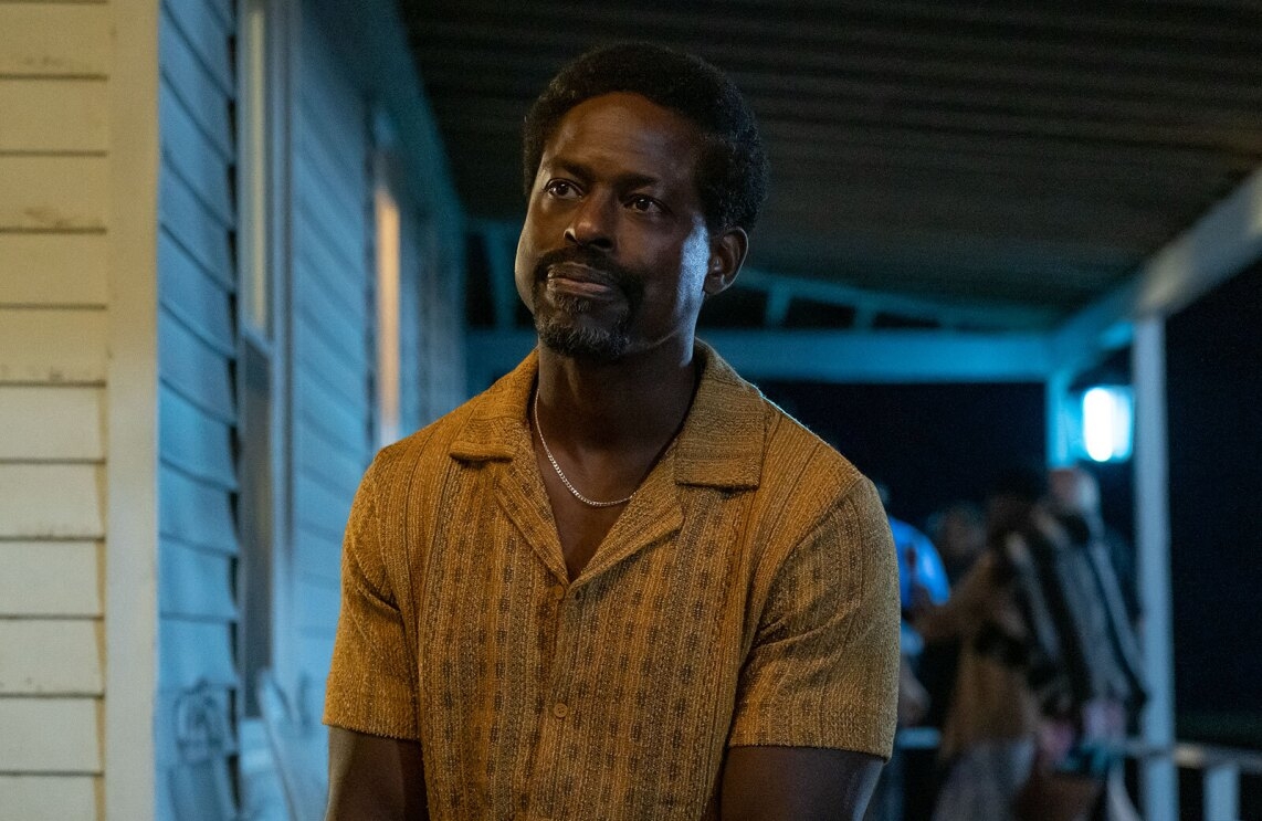 Actor Sterling K Brown sitting on a house front porch and looking off at something behind the camera in a scene from the movie, American Fiction. 
