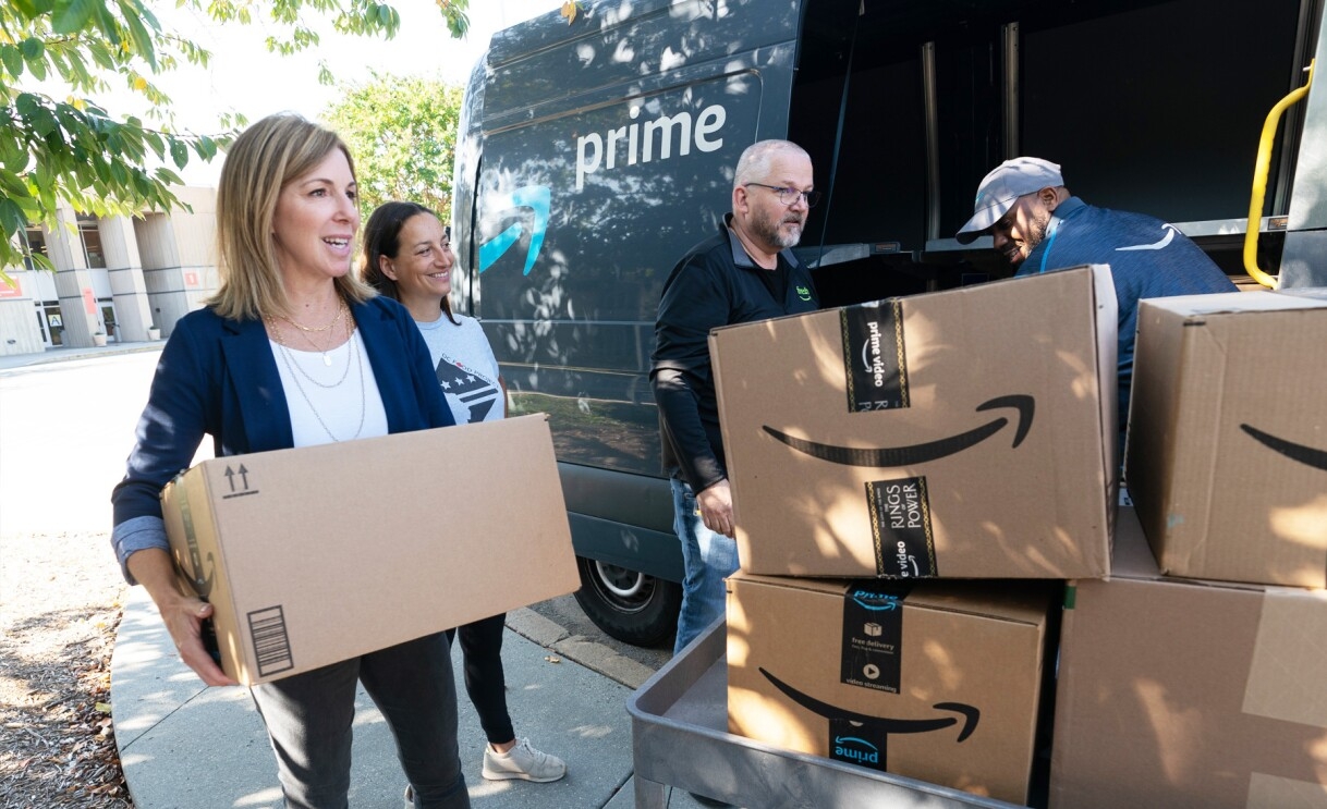 An image of four people removing Amazon boxes from an Amazon delivery van. 