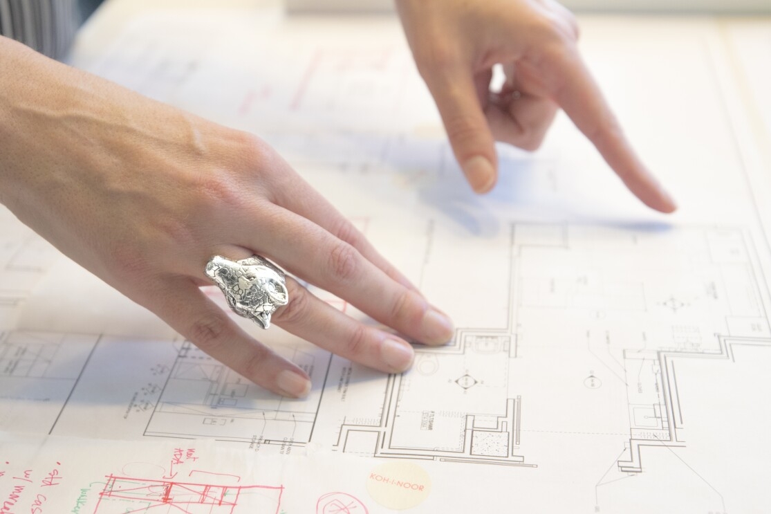A woman's hands, with a large silver giraffe ring, points to architectural design plans. 