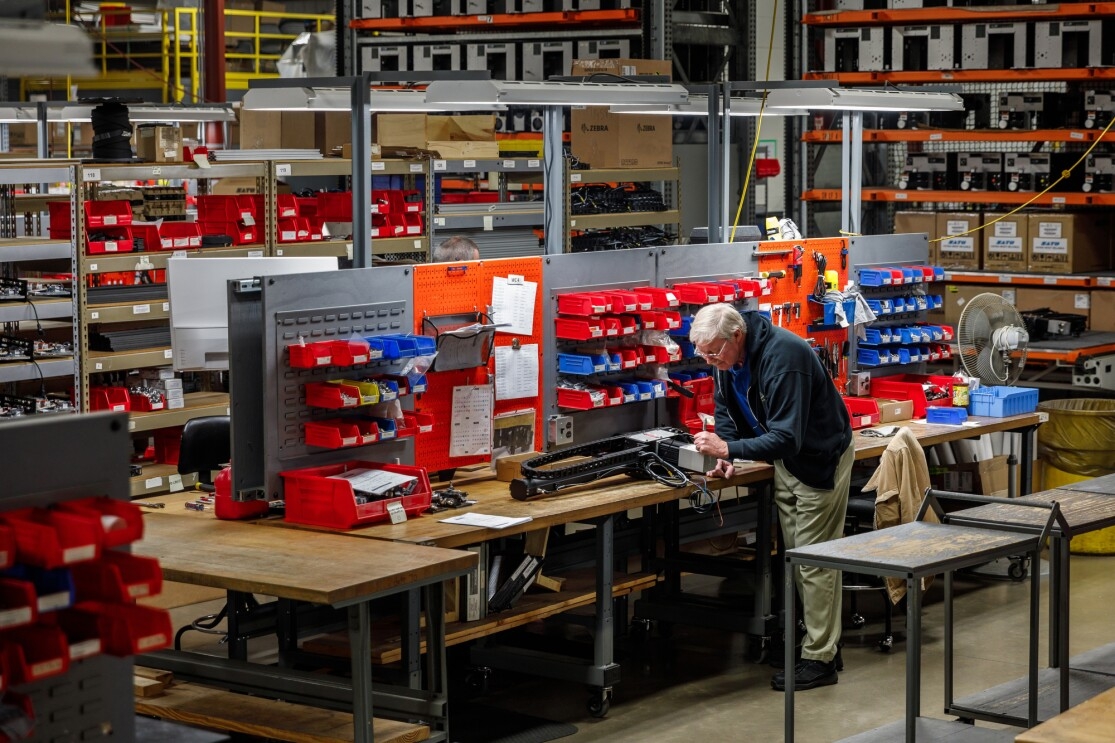 A man works in a manufacturing space with high shelves and workbenches.