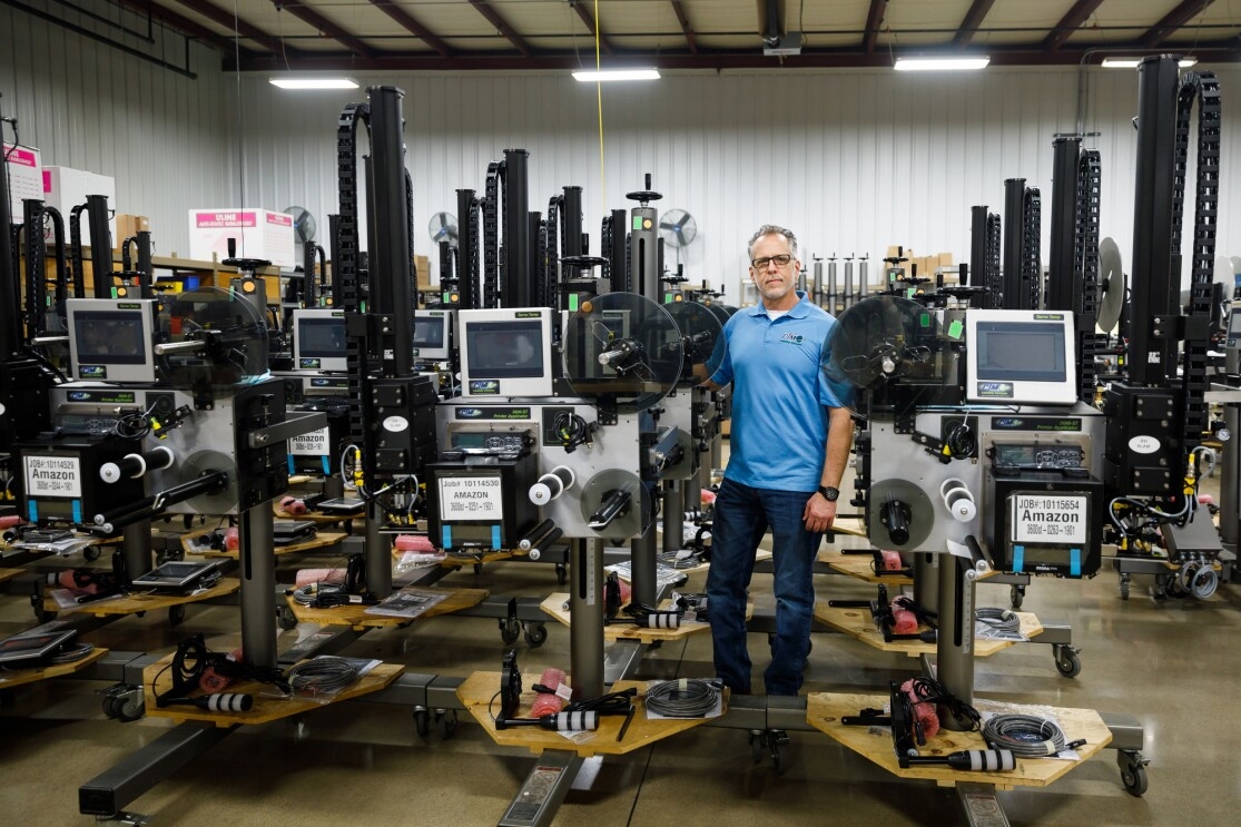 A man in a polo shirt and jeans stands among rows of tall metal machines.