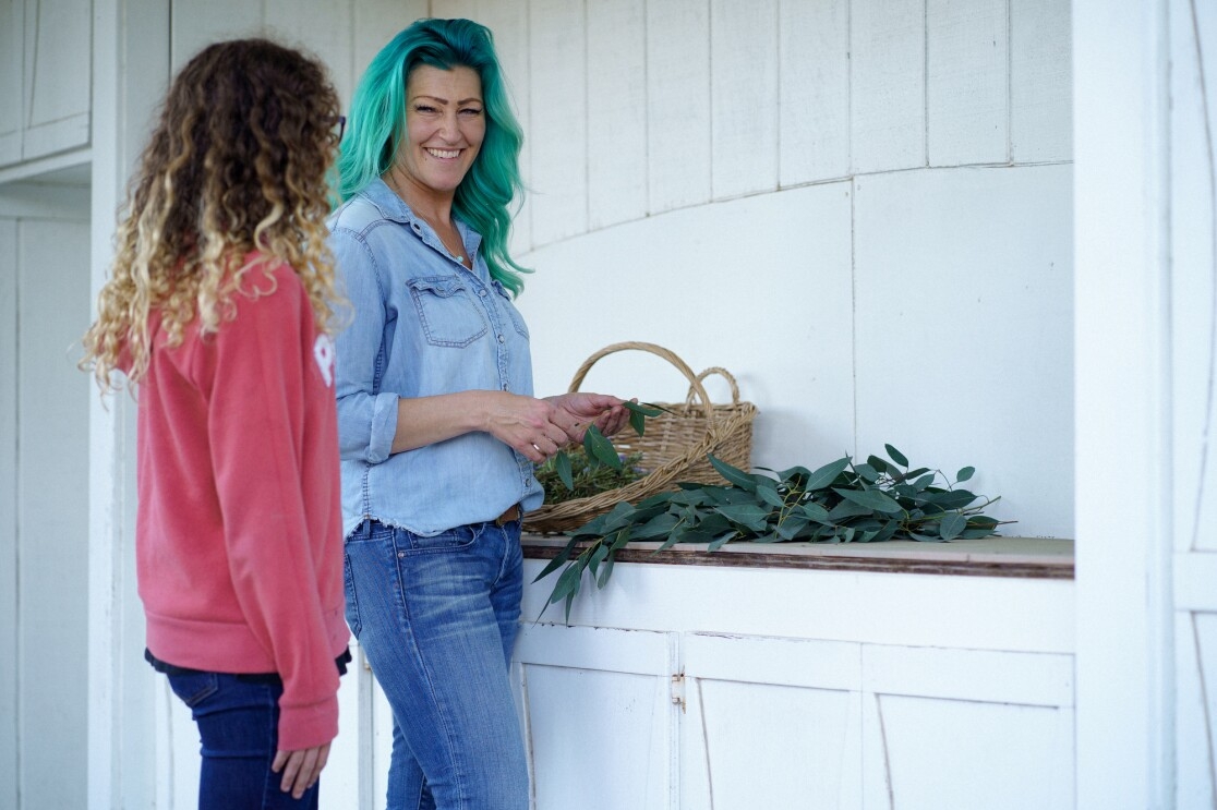 A woman and a girl stand next to a counter that's covered in plants.