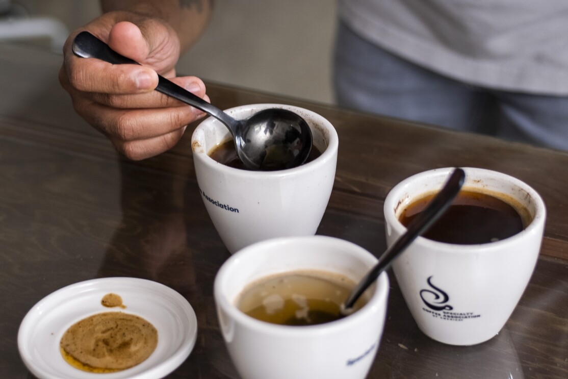 Detail of a person dipping a spoon into a small cup of coffee.