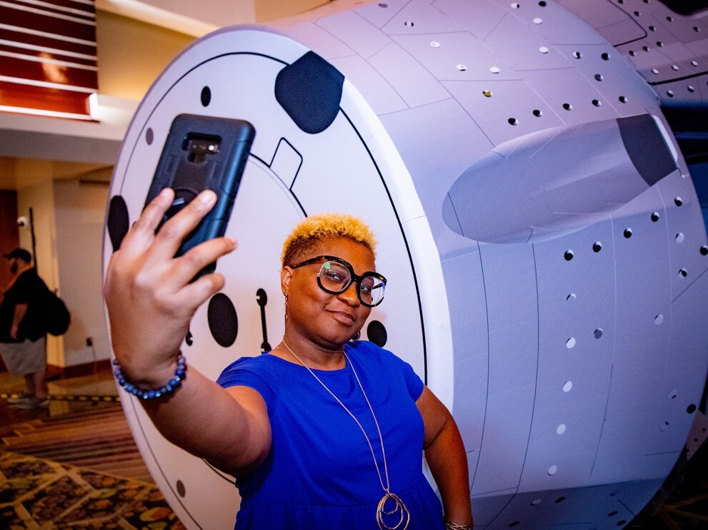 An image of a woman taking a selfie photo in front of the space shuttle mockup at re:MARS 2022.