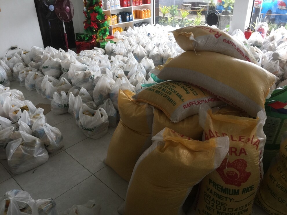 A room full of plastic bags filled food. Gunny sacks filled with rice are stacked to the side of the room.