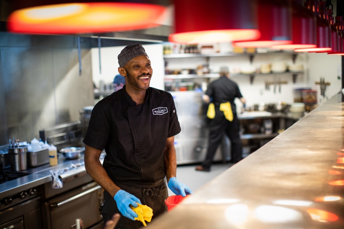 A cook smiles at customers from behind the line at Maslow's, by FareStart, in Seattle, WA.