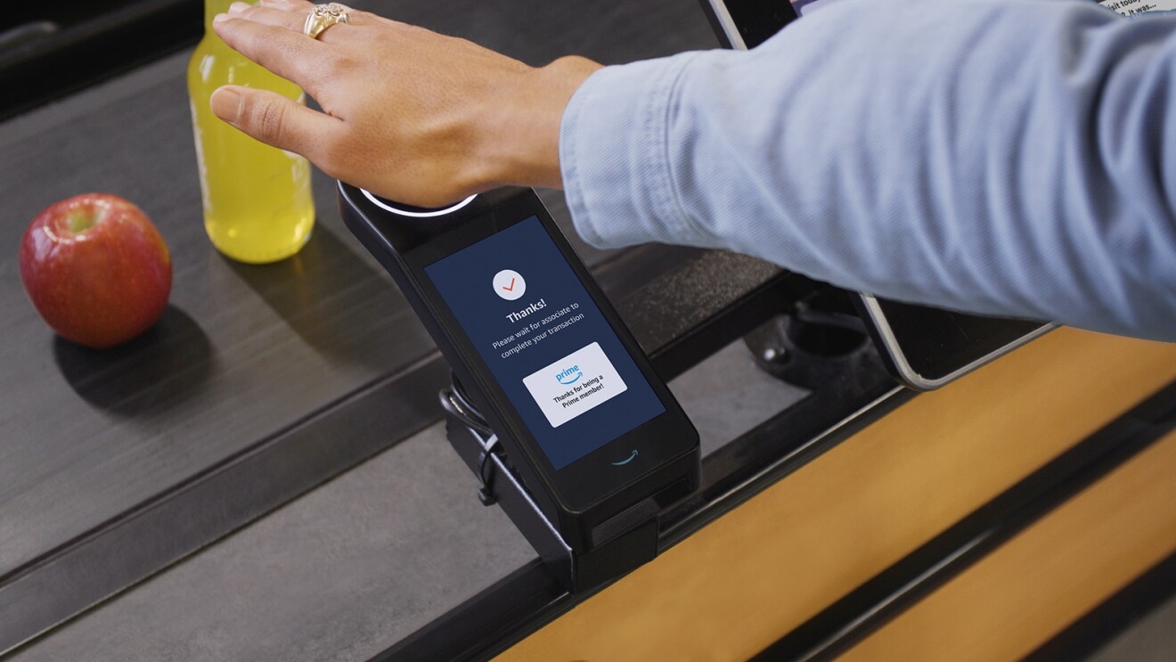 A photo of a customer's hand hovering an Amazon One payment scanner at a Whole Foods check out stand.