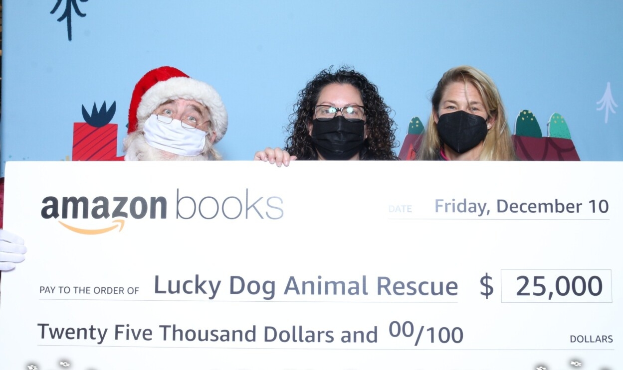 Santa and two women hold up an oversized check made out to Lucky Dog Rescue from Amazon Books for $25,000.