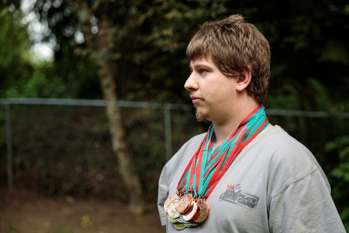 A man in a gray T-shirt stands in profile. He is wearing several medals.
