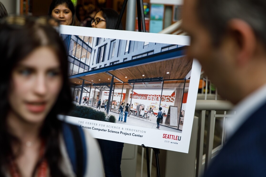 Andy Jassy speaks to a woman, in the background is a rendering of the future Center for Science and Innovation at Seattle University.