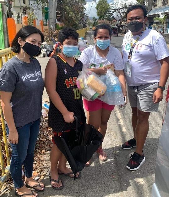 Two Amazon employees pose for a picture with a woman and her son who are both holding plastic bags full of food and water bottles.