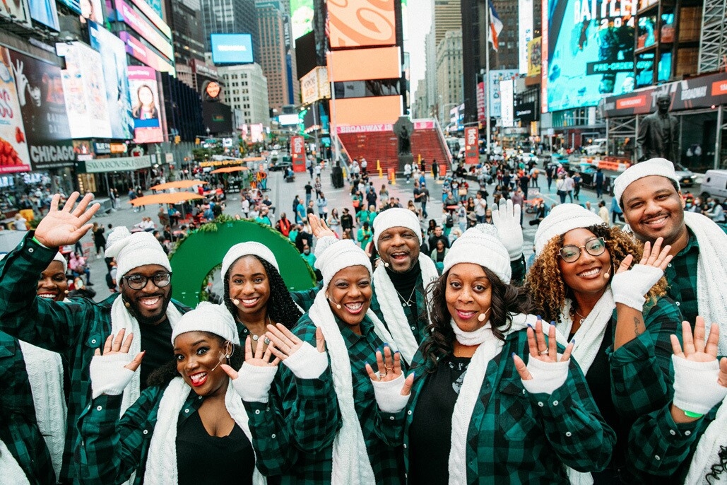 An image of the Harlem Gospel Choir on top of a green double-decker bus singing to crowds in New York.