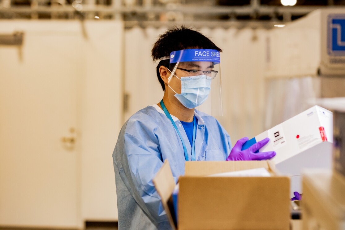 A man wears a face shield, gloves, mask and PPE while handling boxes