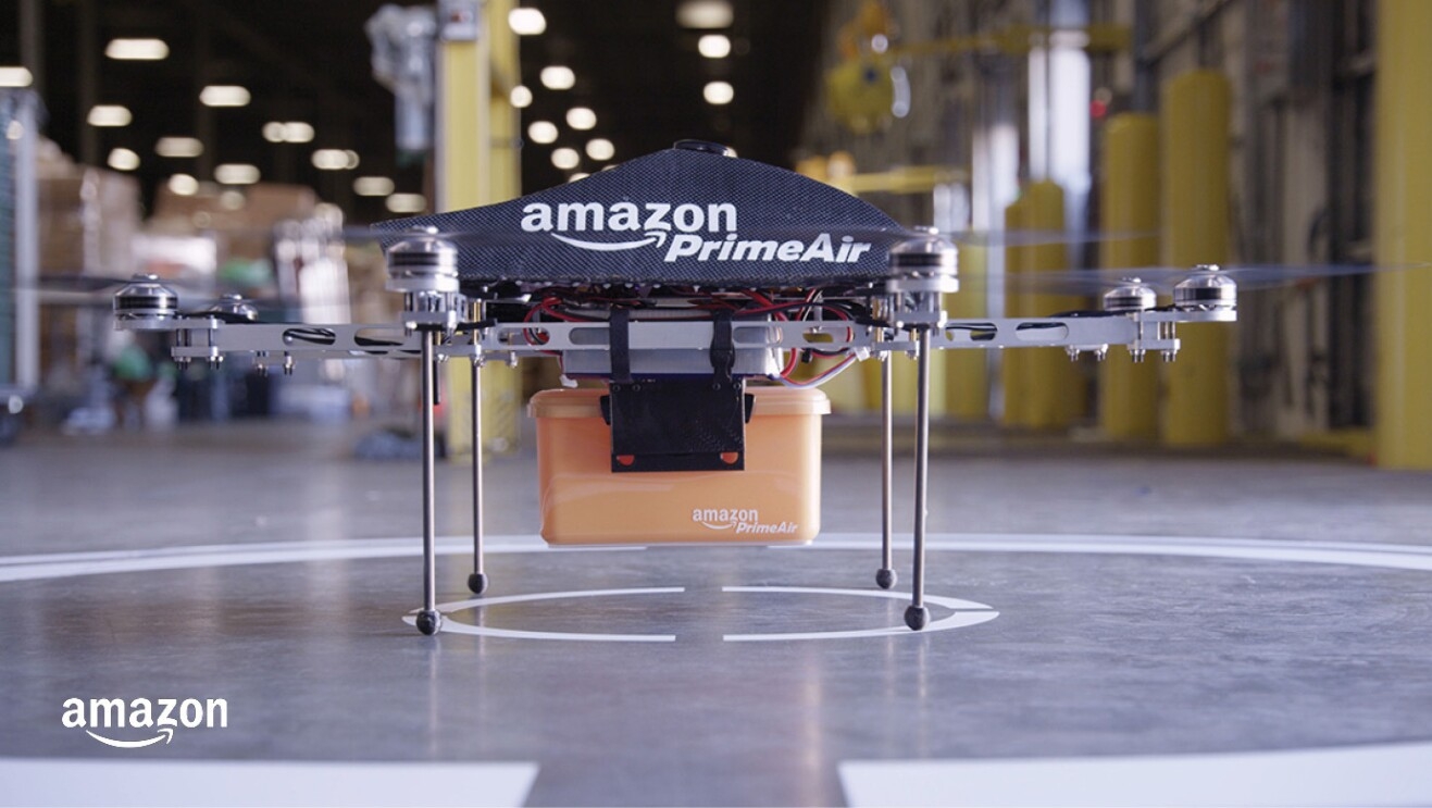 The MK4 drone holds an Amazon Prime Air container and is ready for take off from the inside of a fulfillment center.