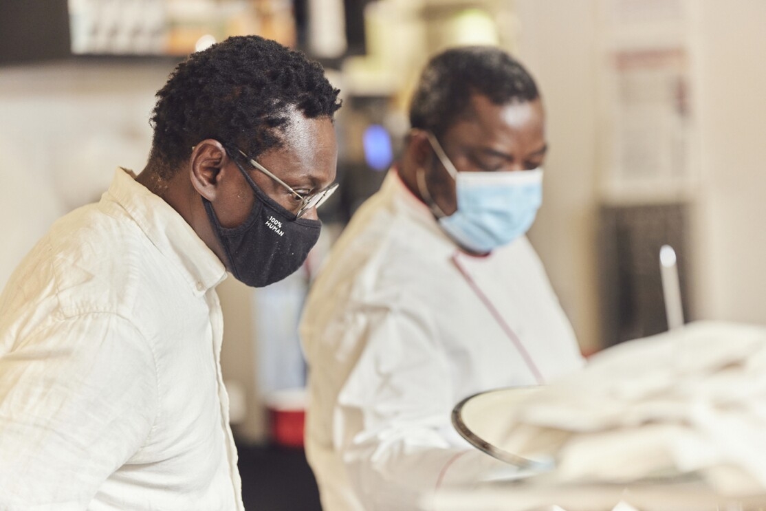 An image of two men wearing masks while cooking together in a restaurant kitchen.