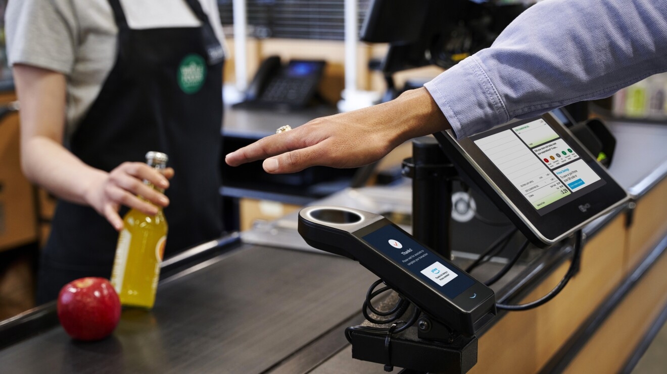A photo of a customer's hand hovering an Amazon One payment scanner at a Whole Foods check out stand.