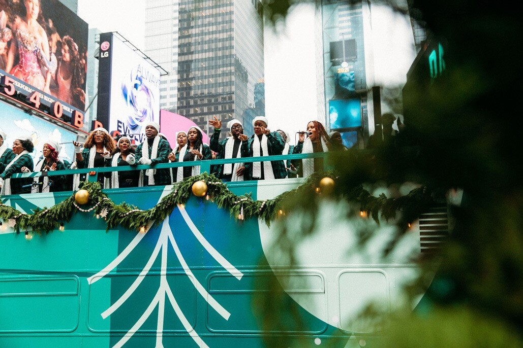An image of the Harlem Gospel Choir on top of a green double-decker bus singing to crowds in New York.