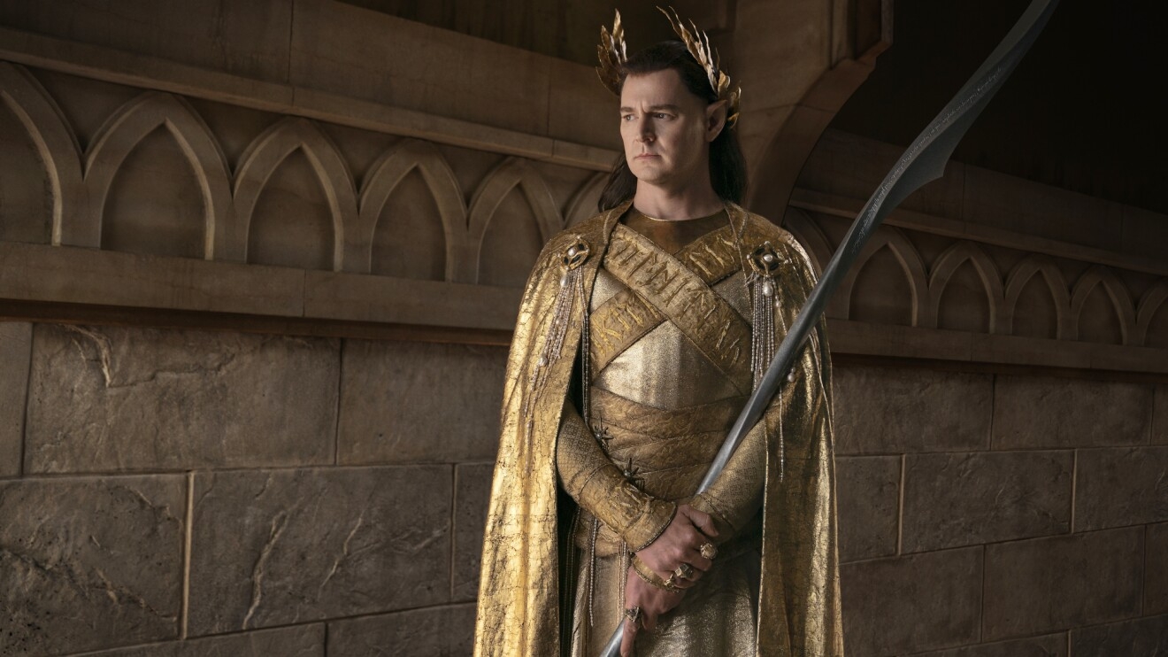 An elf-like male character dressed entirely in gold holds a long, grey metal staff.