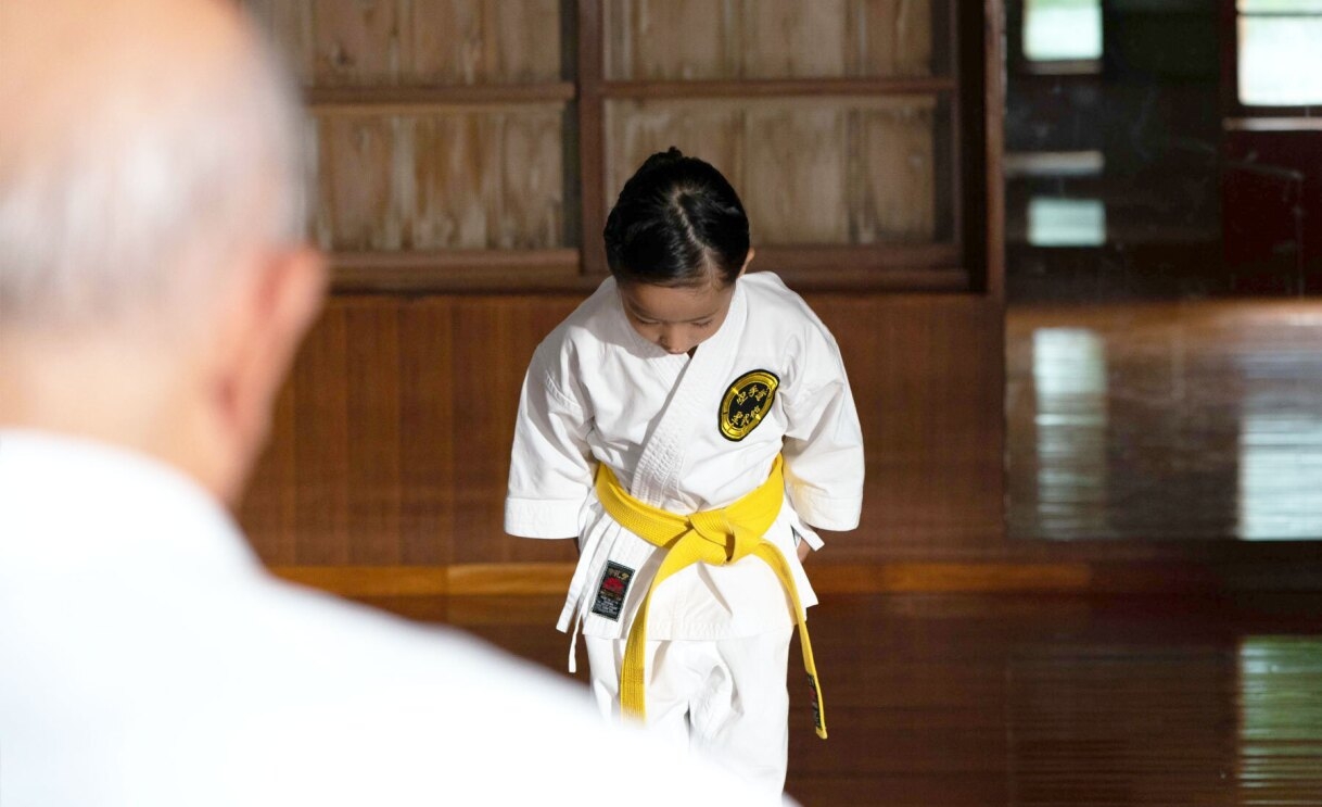 An image of a girl dressed in a karate uniform looking down in a bow.