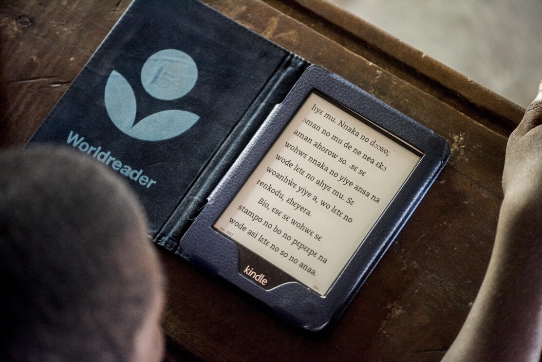The black and white screen of a Kindle on a wooden desk. The Worldreader logo is on the left flyleaf.