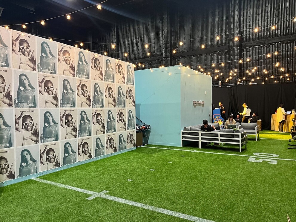 An image of a room with green, football field inspired floors and blue and white walls that show photos of Anitta and 2 Chains on the wallpaper.