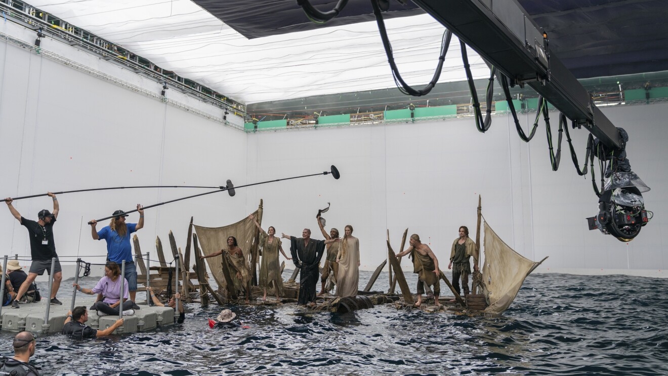Behind-the-scenes of the sea-storm sea where numerous people are on a boat sailing through the water with backstage workers capturing the footage.