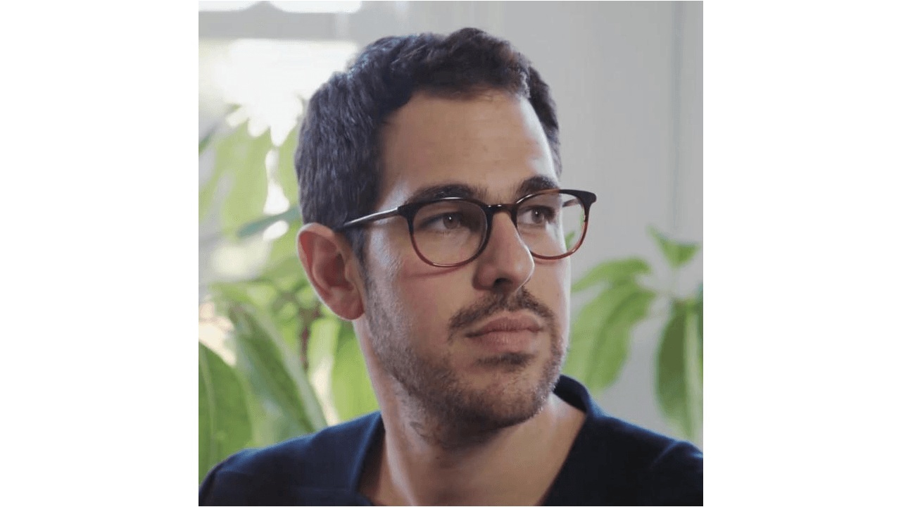 Ezequiel Karpf looks off into the distance and wears eyeglasses. There are houseplants behind him.