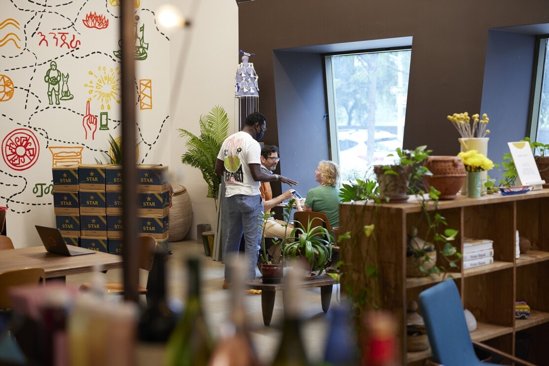 An image of a man standing while talking to two people sitting at a table in a restaurant.