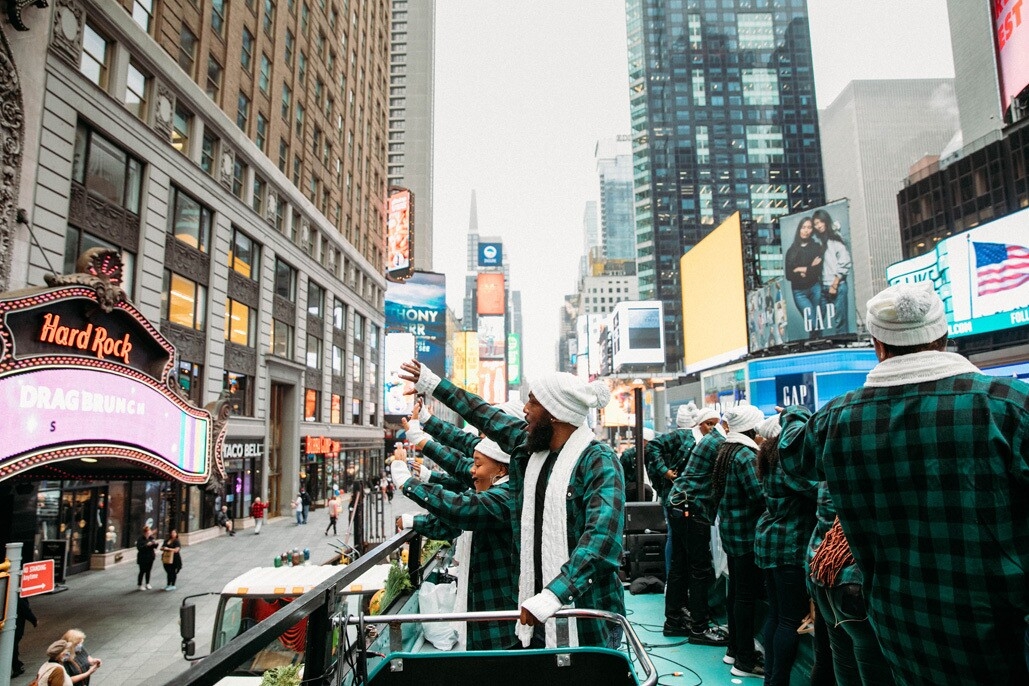 An image of the Harlem Gospel Choir on top of a green double-decker bus singing to crowds in New York.