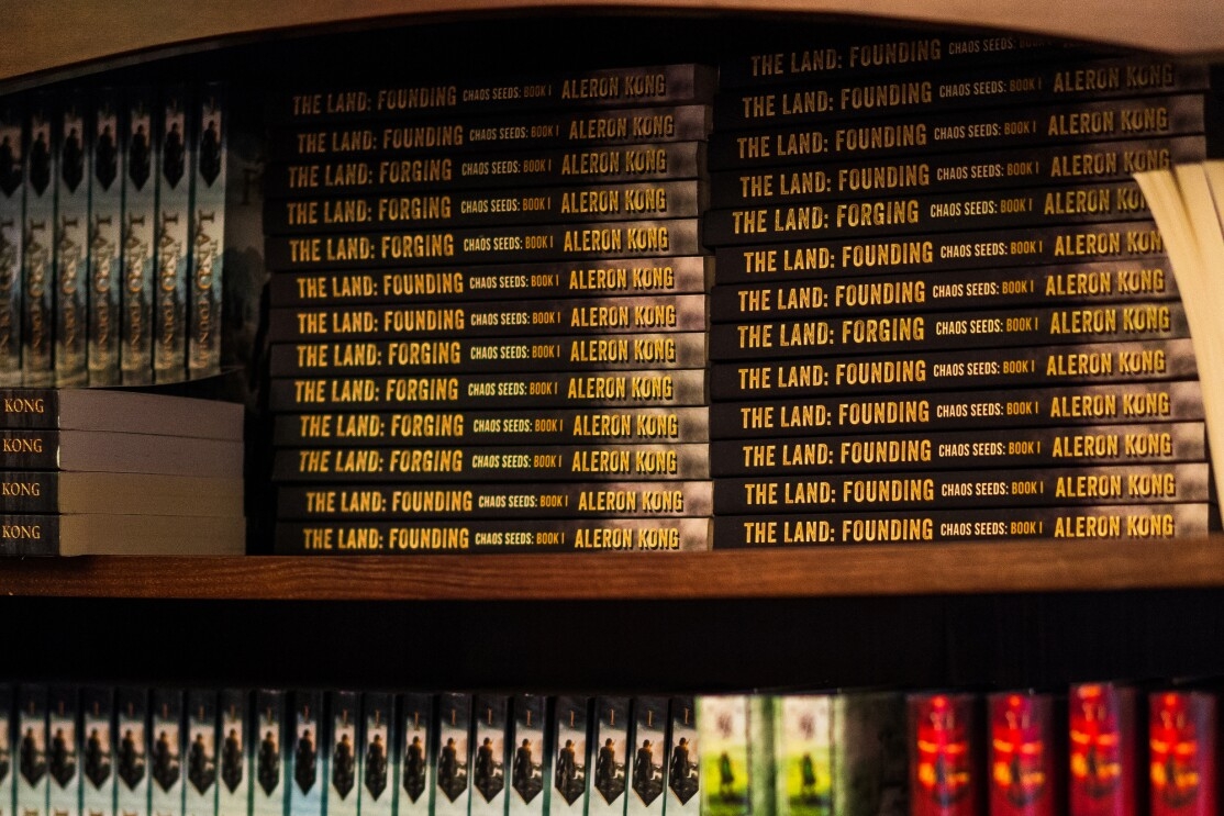 A wood bookcase holds dozens of books bearing the name of author Aleron Kong.