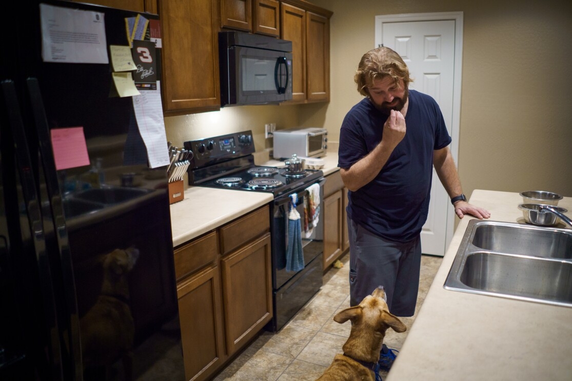 A man and dog stand inside a kitchen.