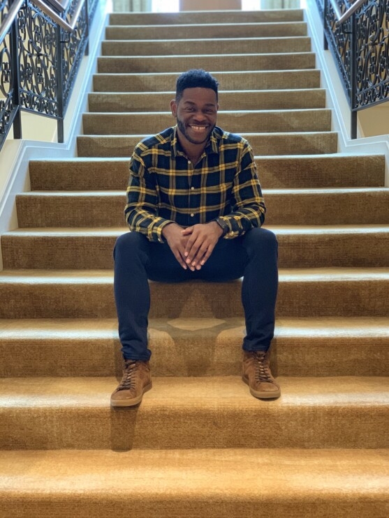 A man sits on a long staircase, while he smiles at the camera.