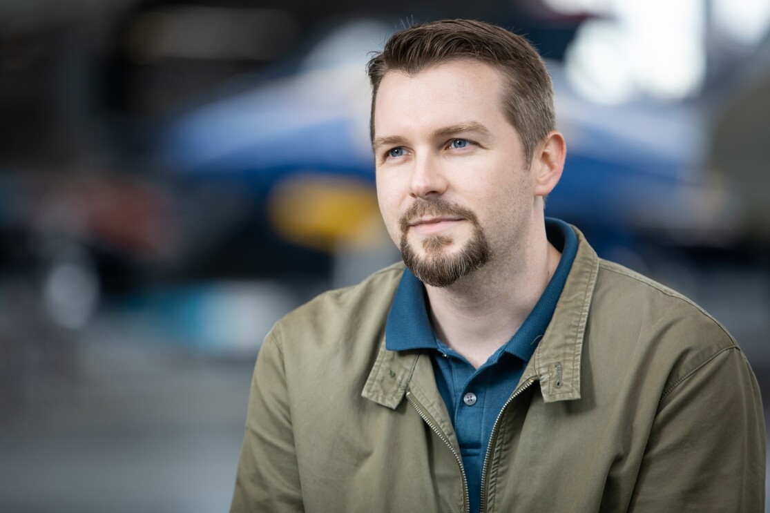 Portrait of man with airplane in background. The man has a goatee and wears a polo shirt and a jacket.