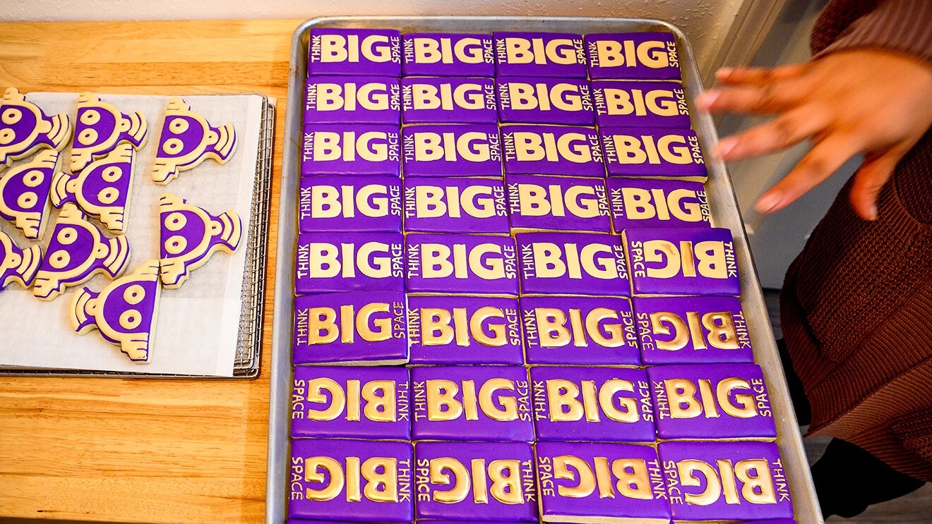 A photo of rectangle-shaped cookies on a baking sheet that are decorated with the AWS Think Big Space logo in icing. There are also cookies decorated as robots featured in the photo.