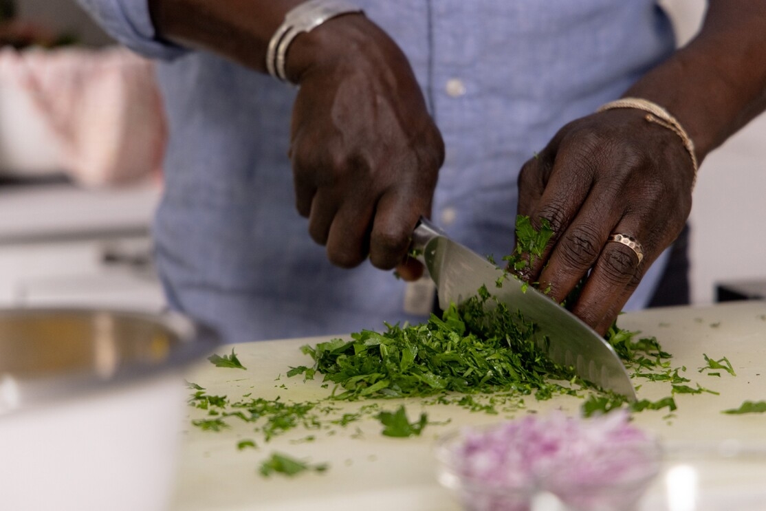 An image of a man chopping spinach with a large cutting knife. The image is zoomed in to focus on his hands. 