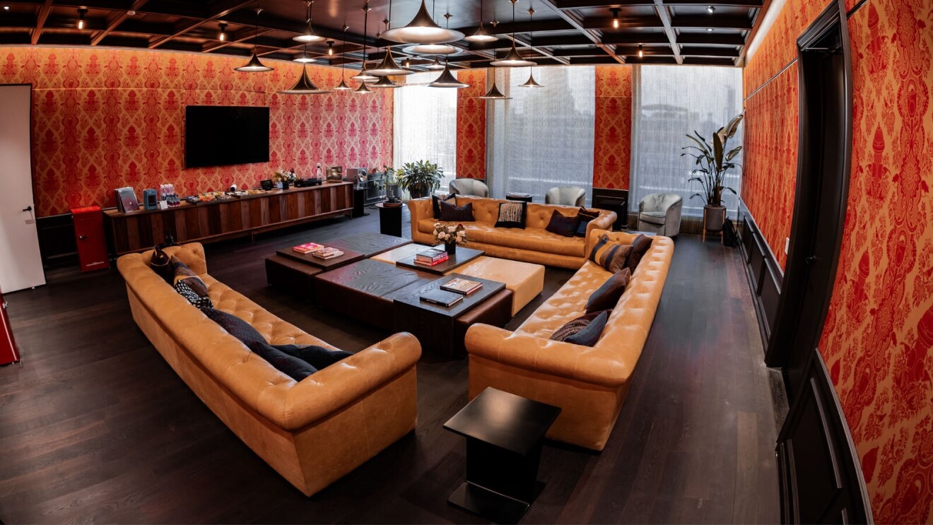 A living room area with a TV, two large couches, and a large coffee table. The wallpaper and furniture are all different shades of orang and brown.