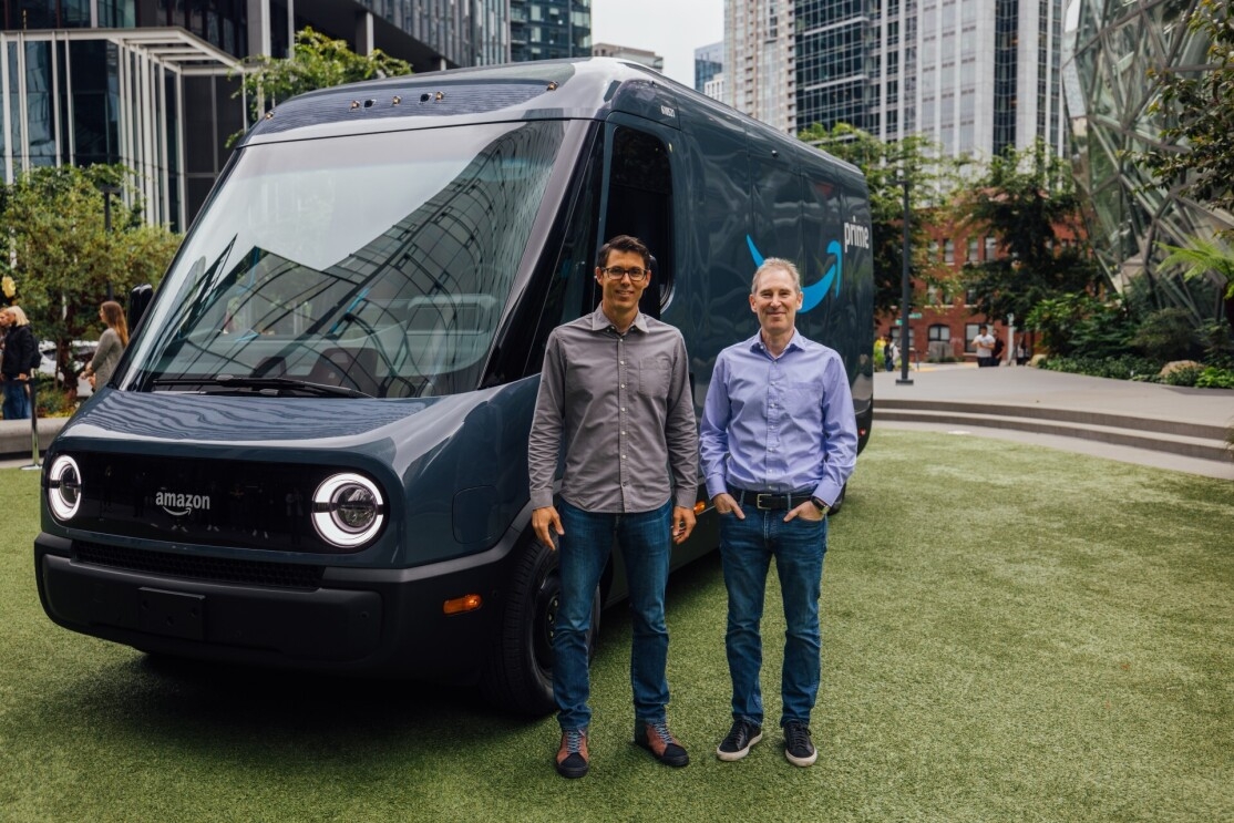 Andy Jassy and RJ Scaringe stand side-by-side in front of a Rivian Amazon delivery vehicle that is parked outside the Spheres at Amazon headquarters.