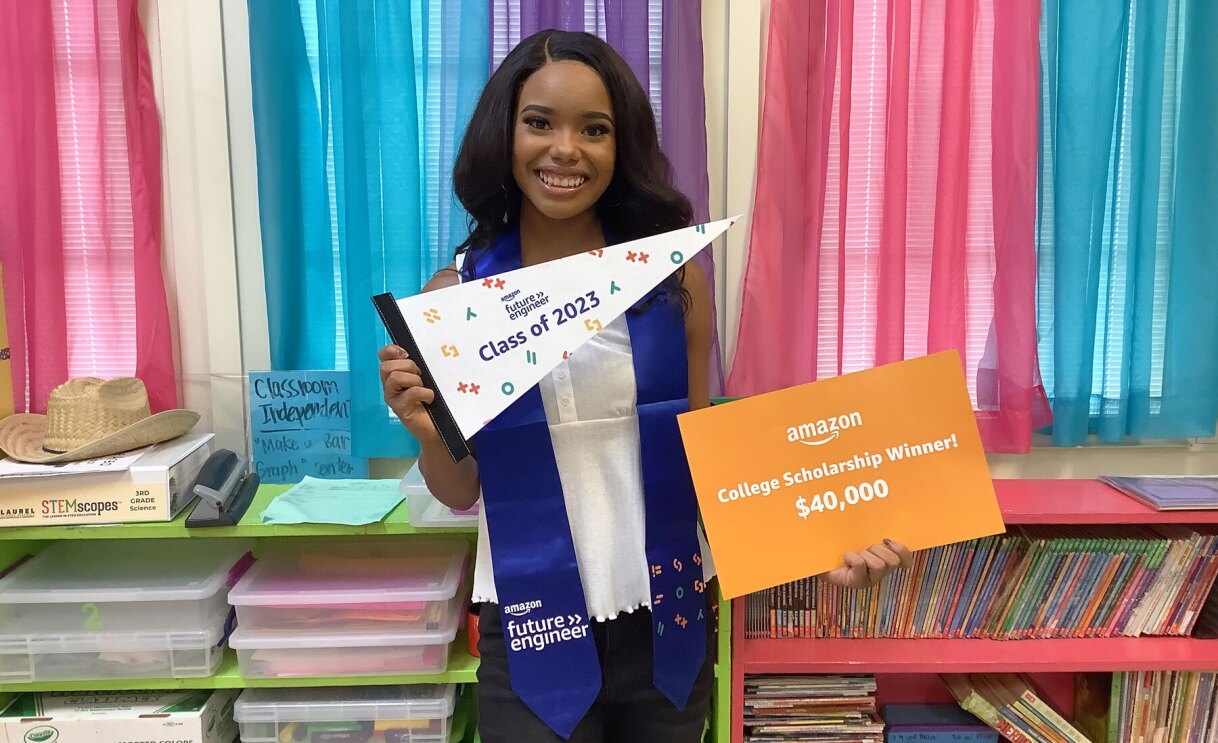 An image of Micah Hill, a 2023 Amazon Future Engineer Scholarship recipient, holding out a sign that reads "Amazon College Scholarship Winner."