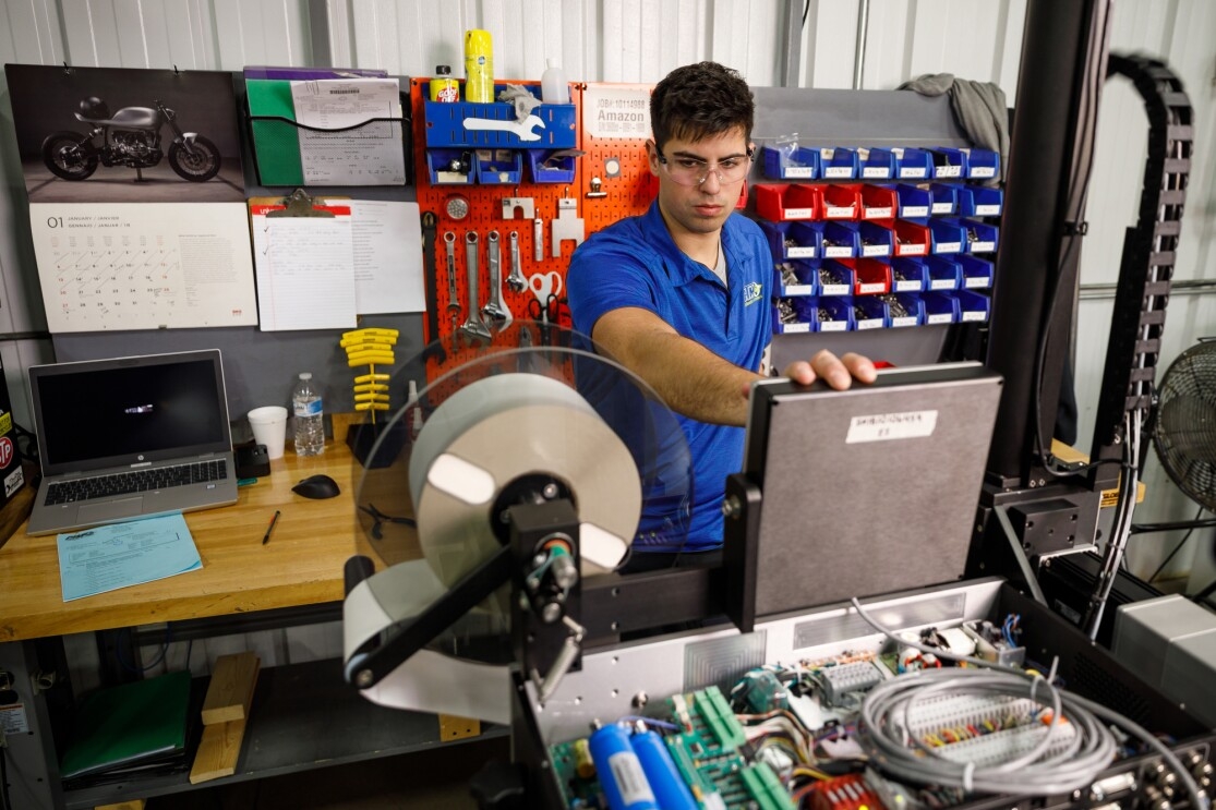 A man wearing safety glasses looks at a device that includes a spool that holds labels.