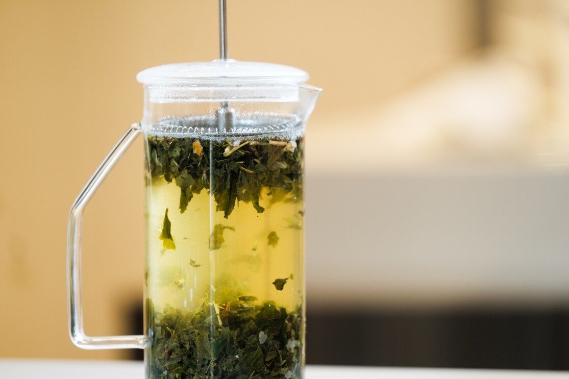 Tea leaves float in hot water in a press-style teapot.