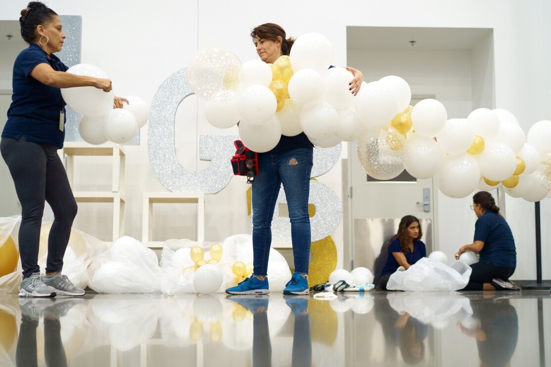 Women work to assemble decorations made out of white, gold, and sparkly balloons.