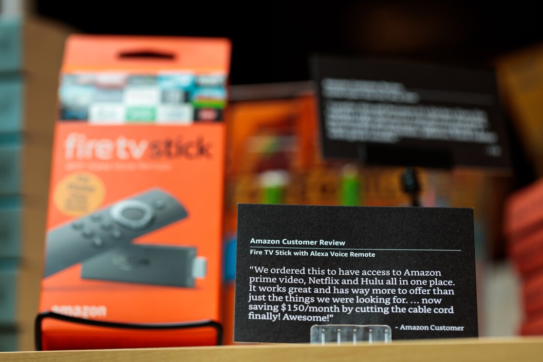A black "customer review card" inside the Amazon 4-star store in New York City. The review is for an Amazon Fire TV stick with Alexa Voice Remote. 