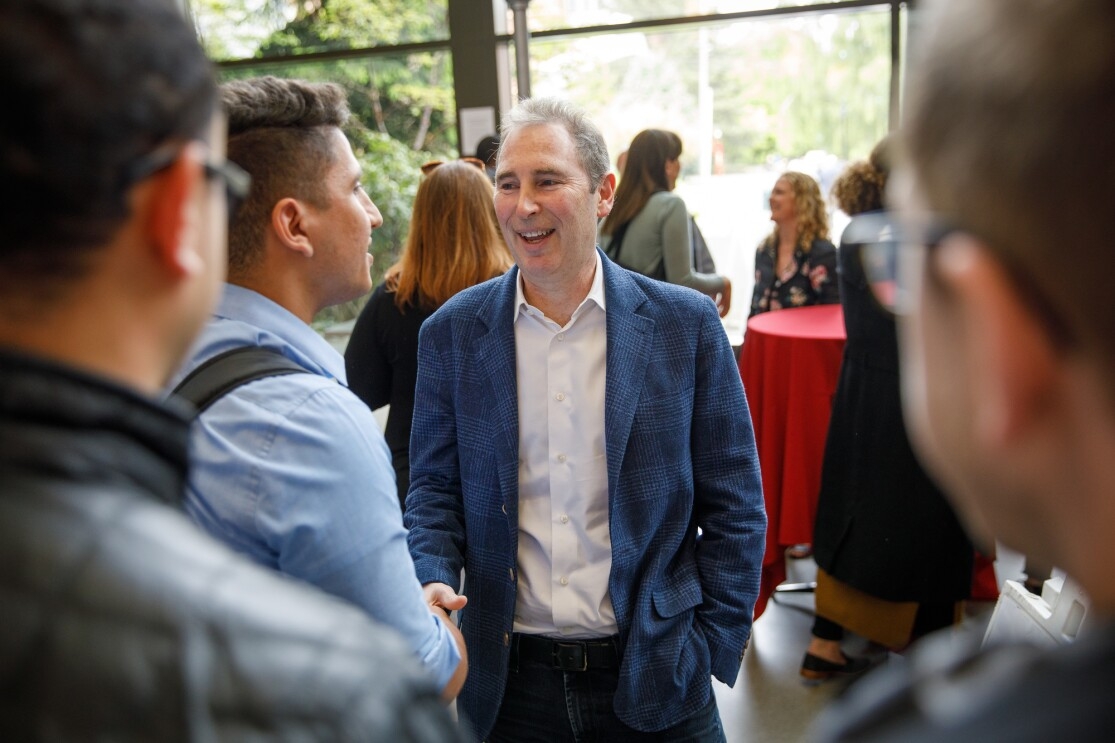 An image of Andy Jassy at an event at Seattle University in 2019. He is speaking with a group of students at a social gathering and smiling while shaking one student's hand.