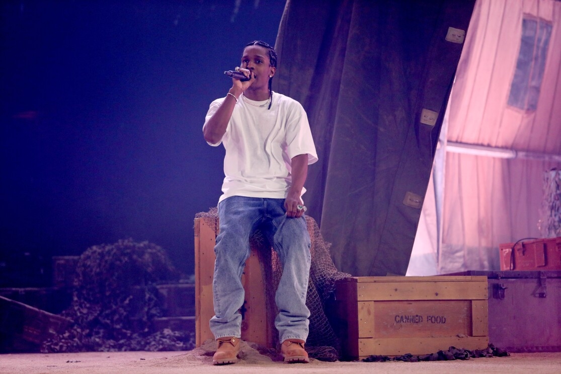 ASAP Rocky sits on a prop box on a stage set singing into the microphone