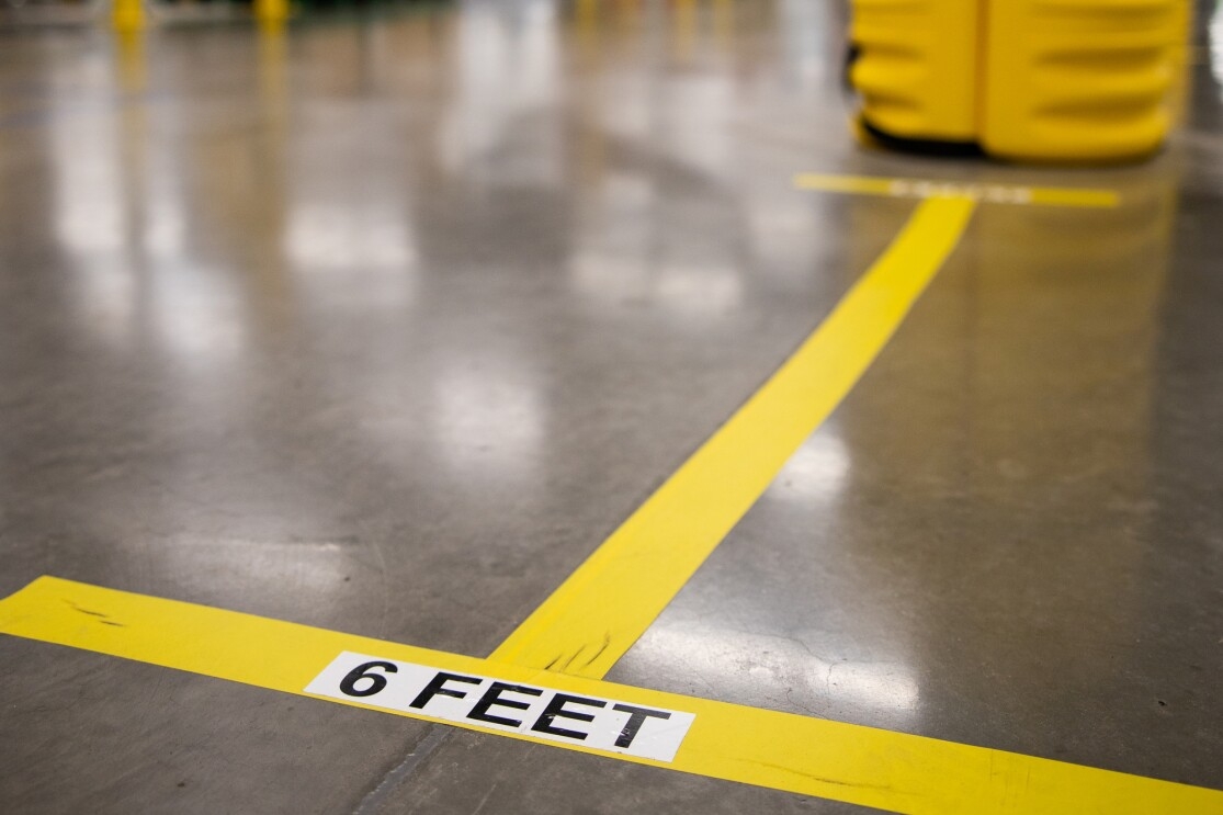 Markings on a concrete floor in a workplace say "6 FEET"